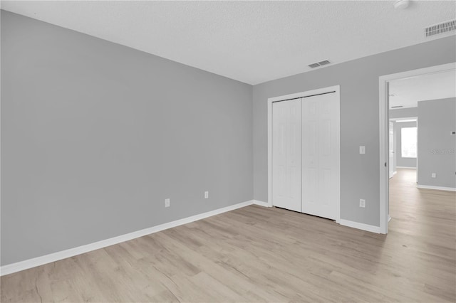 unfurnished bedroom featuring light wood finished floors, baseboards, a closet, and a textured ceiling