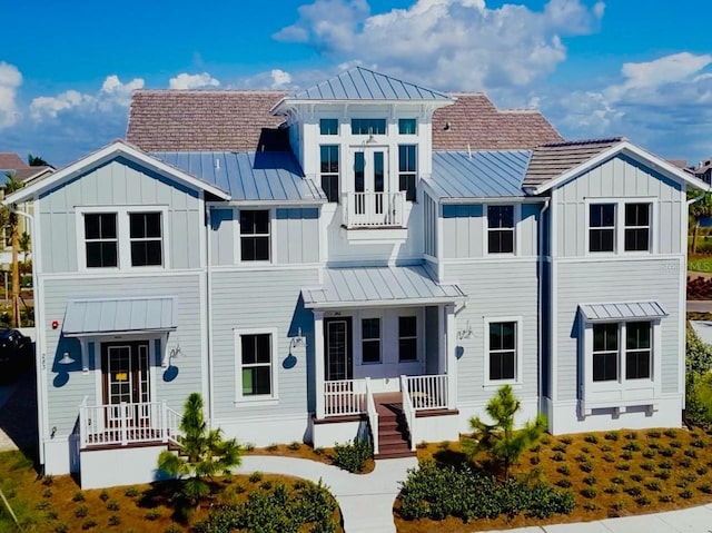 view of front of house featuring board and batten siding, covered porch, a standing seam roof, metal roof, and a balcony
