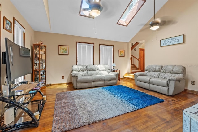 living room featuring stairway, ceiling fan, wood finished floors, and vaulted ceiling with skylight