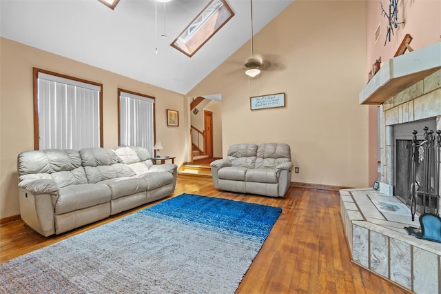 living room featuring wood finished floors, high vaulted ceiling, stairway, a ceiling fan, and a skylight