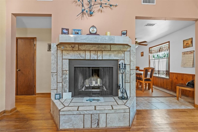 details featuring a fireplace with raised hearth, ceiling fan, visible vents, and wood finished floors