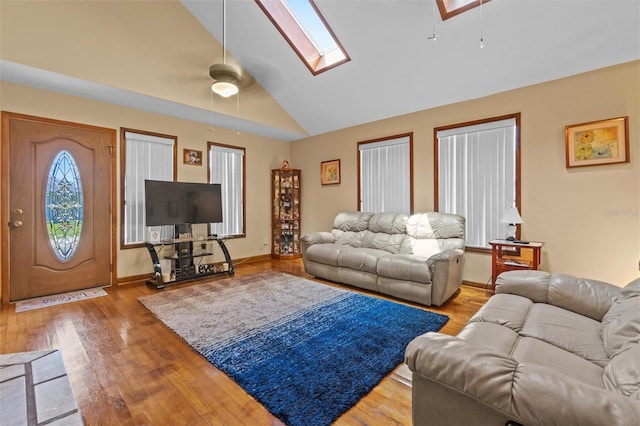 living area featuring baseboards, lofted ceiling with skylight, wood finished floors, and ceiling fan