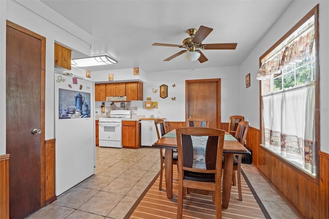 dining space featuring ceiling fan, a wainscoted wall, wooden walls, and light tile patterned floors