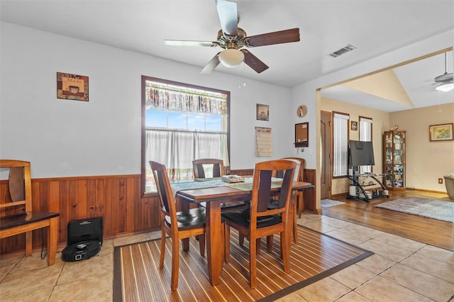 dining area featuring visible vents, wainscoting, wooden walls, a ceiling fan, and light tile patterned floors