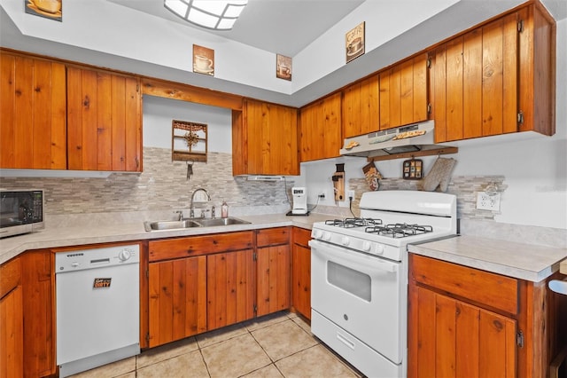 kitchen with backsplash, a sink, light countertops, under cabinet range hood, and white appliances
