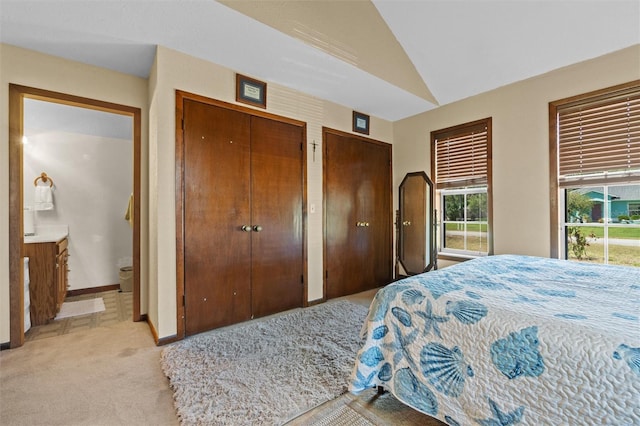 bedroom featuring baseboards, multiple closets, vaulted ceiling, and light carpet