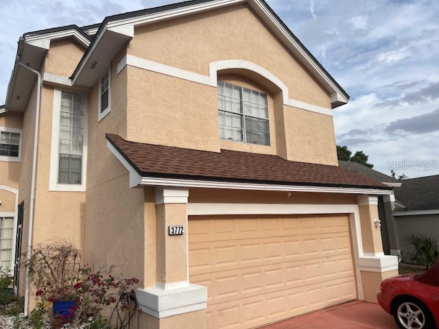 traditional home featuring stucco siding, roof with shingles, and an attached garage