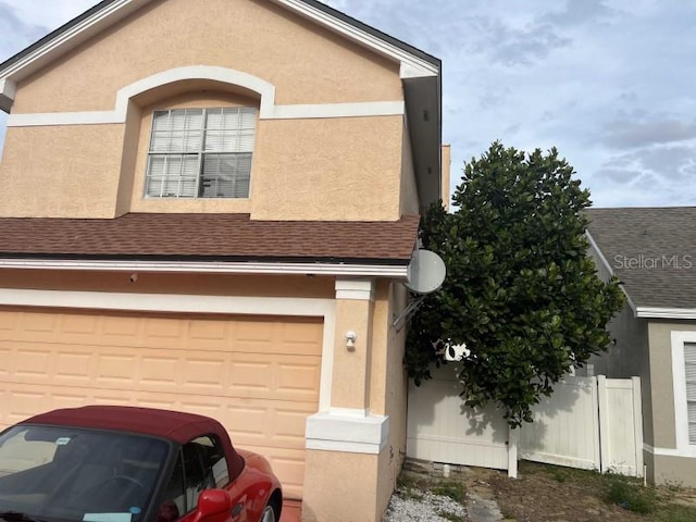 view of front facade with a garage, fence, a shingled roof, and stucco siding