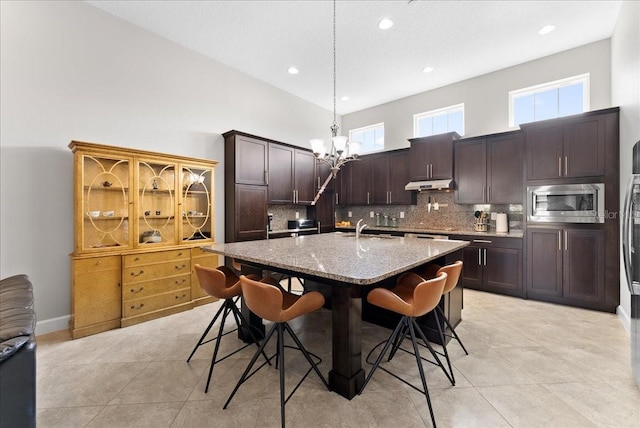 13865 Granger Ave, Orlando, FL 32827 - kitchen featuring decorative backsplash, stainless steel microwave, under cabinet range hood, a chandelier, and a sink