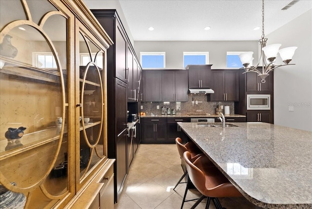 13865 Granger Ave, Orlando, FL 32827 - kitchen with light stone countertops, a notable chandelier, stainless steel microwave, tasteful backsplash, and under cabinet range hood