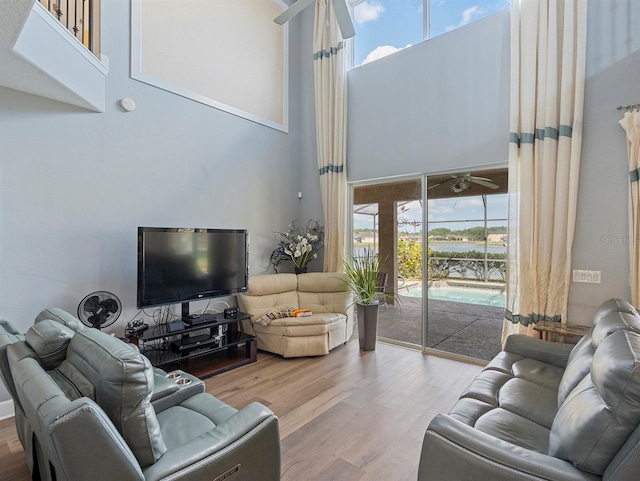 living room with ceiling fan, a high ceiling, and wood finished floors