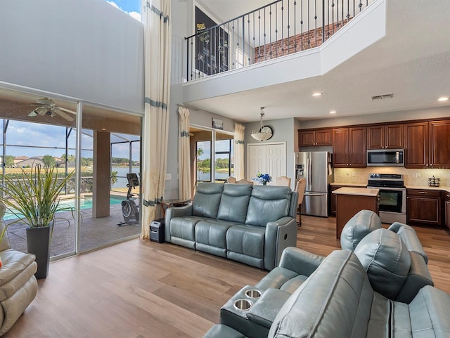 living area with a ceiling fan, light wood-style flooring, recessed lighting, visible vents, and a high ceiling
