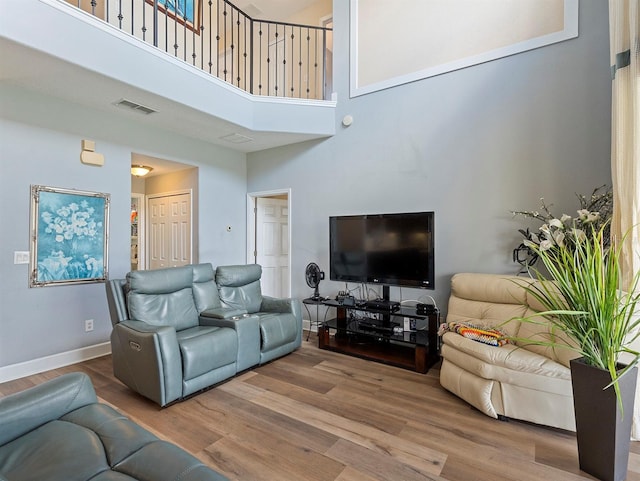 living area featuring baseboards, visible vents, a towering ceiling, and wood finished floors