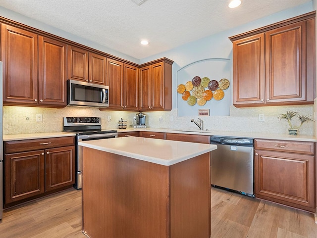 kitchen with stainless steel appliances, a center island, a sink, light countertops, and light wood-type flooring