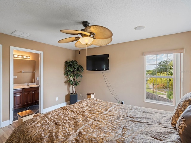 bedroom with a textured ceiling, ensuite bath, a sink, and wood finished floors