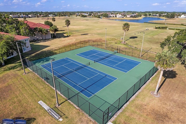 view of tennis court with a water view, golf course view, fence, and a lawn
