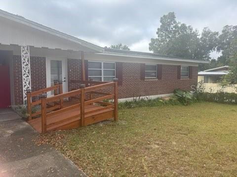 404 E Kentucky Ave, Deland, FL 32724 - back of property featuring brick siding, a lawn, and a wooden deck