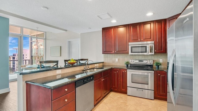 kitchen with appliances with stainless steel finishes, tasteful backsplash, a sink, a peninsula, and reddish brown cabinets
