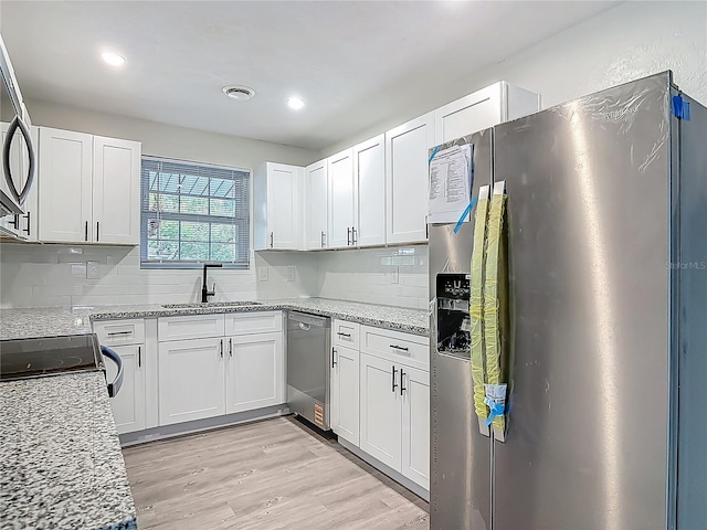 1298 Scottsdale Dr, Ormond Beach, FL 32174 - kitchen with appliances with stainless steel finishes, tasteful backsplash, a sink, white cabinetry, and light wood-type flooring