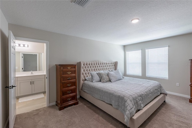 bedroom featuring baseboards, a sink, a textured ceiling, and light carpet