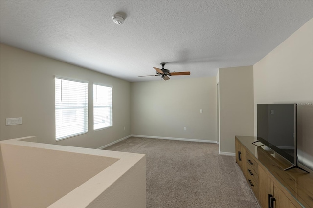 unfurnished living room with light colored carpet, a textured ceiling, ceiling fan, and baseboards