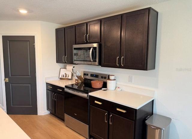 kitchen featuring stainless steel appliances, light countertops, light wood-style floors, and dark brown cabinetry