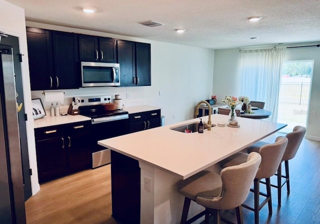 kitchen with stainless steel microwave, electric range oven, a sink, a kitchen bar, and a textured ceiling
