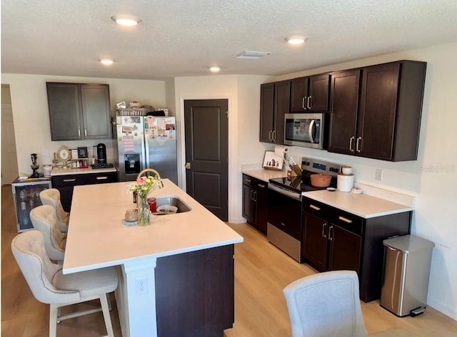 kitchen featuring stainless steel appliances, a sink, light countertops, a breakfast bar area, and a kitchen island with sink