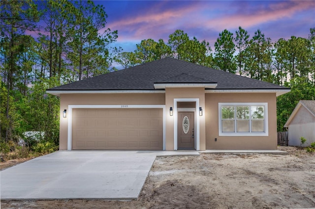 view of front of home with a shingled roof, stucco siding, an attached garage, and driveway