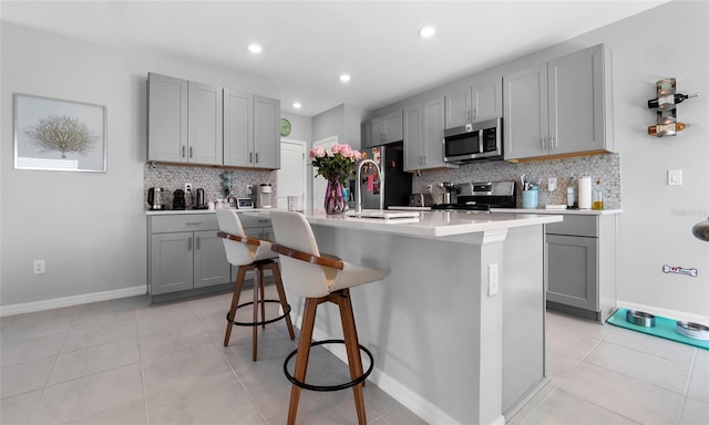 kitchen featuring appliances with stainless steel finishes, gray cabinets, backsplash, a sink, and a breakfast bar area