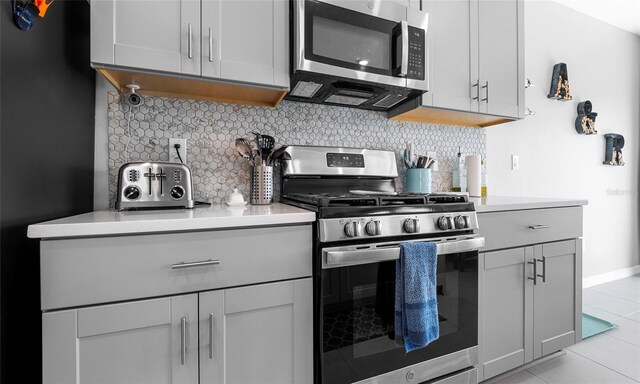kitchen with stainless steel appliances, gray cabinets, backsplash, and light countertops