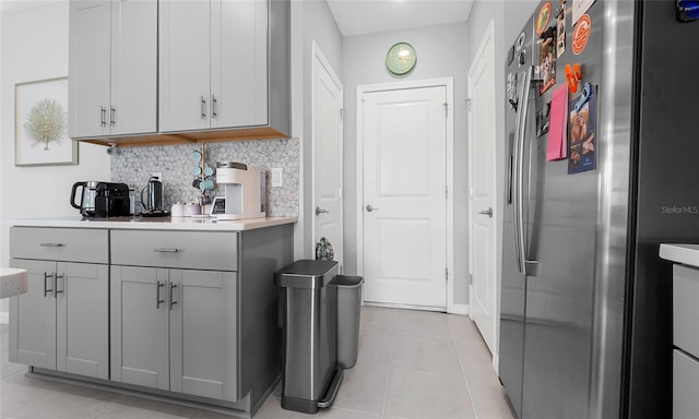 kitchen with freestanding refrigerator, gray cabinetry, decorative backsplash, light countertops, and light tile patterned flooring
