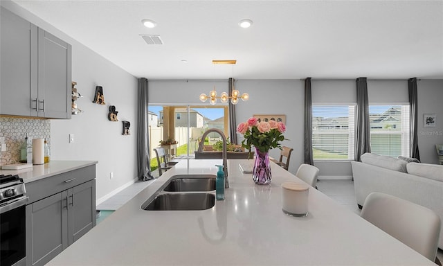 kitchen featuring gray cabinets, a sink, light countertops, a chandelier, and decorative backsplash