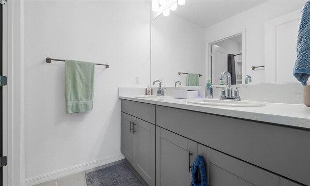 full bathroom with baseboards, tile patterned flooring, double vanity, and a shower