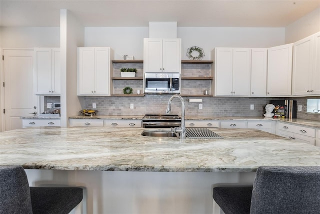 kitchen with open shelves, appliances with stainless steel finishes, a sink, and a kitchen bar