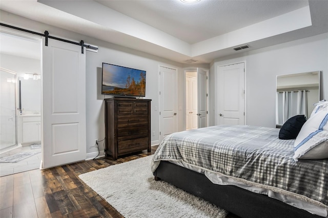 bedroom featuring visible vents, a barn door, connected bathroom, a tray ceiling, and dark wood finished floors