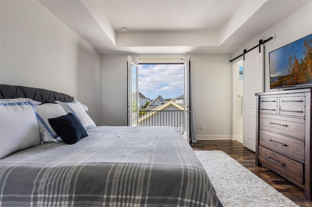 bedroom with access to outside, a barn door, a raised ceiling, baseboards, and dark wood-type flooring