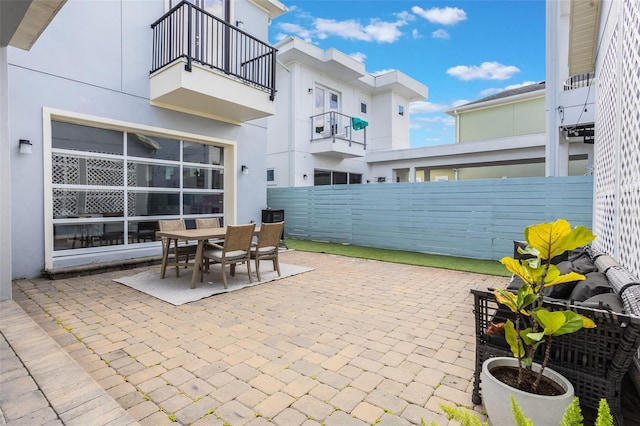 view of patio with outdoor dining area, fence, and a balcony