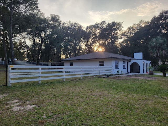 property exterior at dusk featuring fence private yard, a lawn, stucco siding, and a chimney