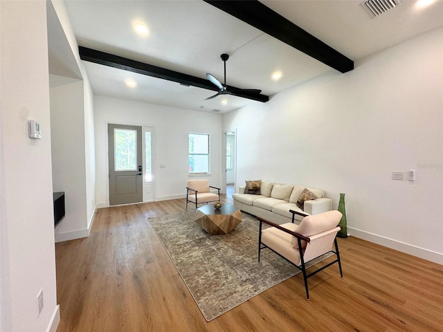 living area with light wood-style flooring, a ceiling fan, visible vents, baseboards, and beamed ceiling