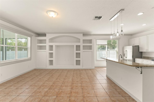 kitchen featuring refrigerator with ice dispenser, a kitchen bar, pendant lighting, ornamental molding, and light stone countertops