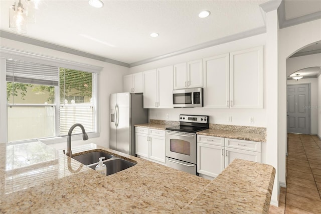 kitchen featuring appliances with stainless steel finishes, a sink, arched walkways, light tile patterned floors, and white cabinetry
