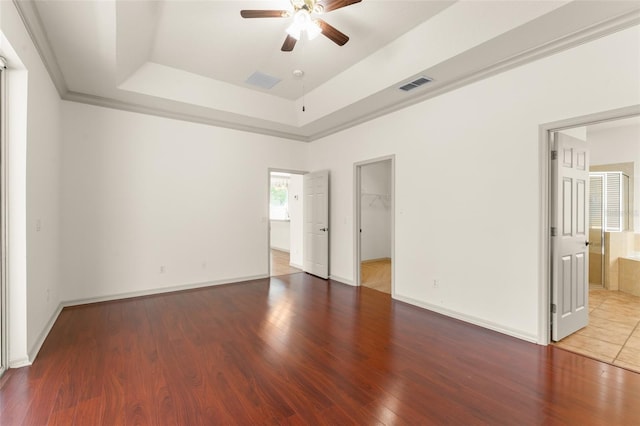 unfurnished bedroom with a raised ceiling, wood finished floors, a spacious closet, and baseboards
