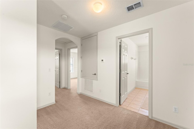 hallway with arched walkways, light carpet, light tile patterned floors, and baseboards