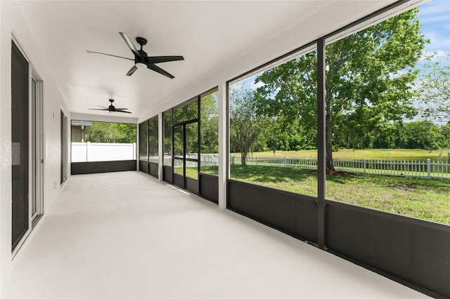 unfurnished sunroom with ceiling fan and view of wooded area