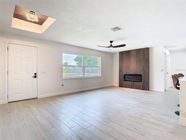 unfurnished living room featuring ceiling fan, a large fireplace, light wood-style flooring, and baseboards