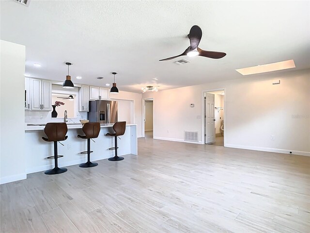 unfurnished living room featuring ceiling fan, light wood-type flooring, baseboards, and a sink