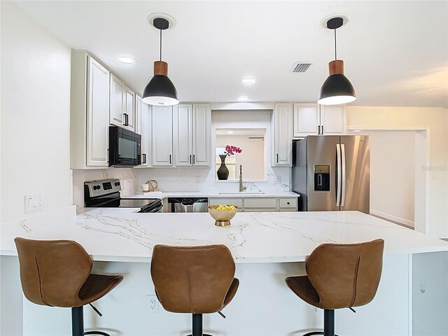 kitchen featuring stainless steel appliances, a sink, a peninsula, a breakfast bar area, and decorative light fixtures