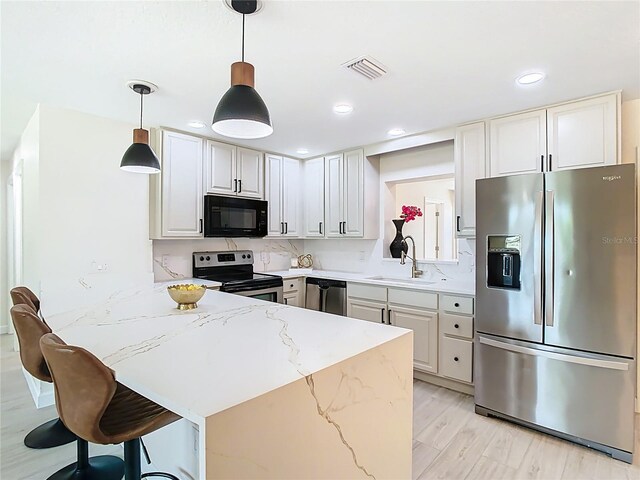 kitchen featuring appliances with stainless steel finishes, a sink, a peninsula, recessed lighting, and light stone counters