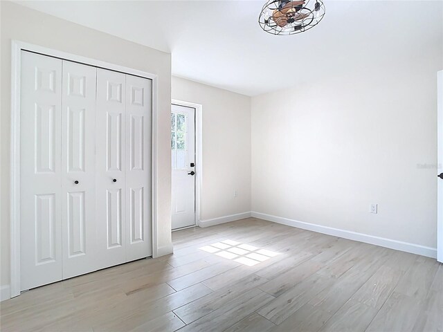 unfurnished bedroom featuring light wood finished floors, baseboards, and a closet